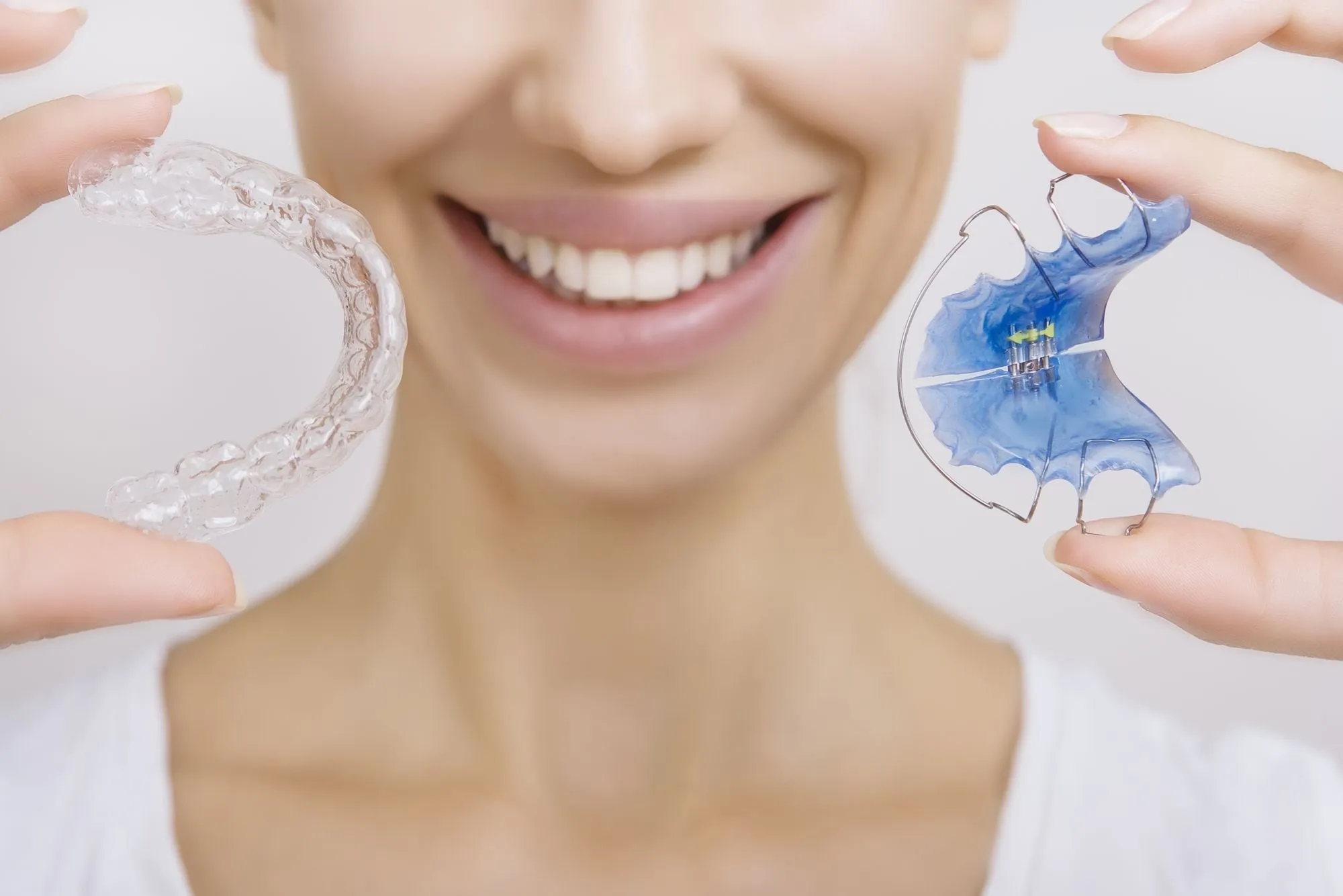 A clear retainer and a removable plate retainer held up beside a smile